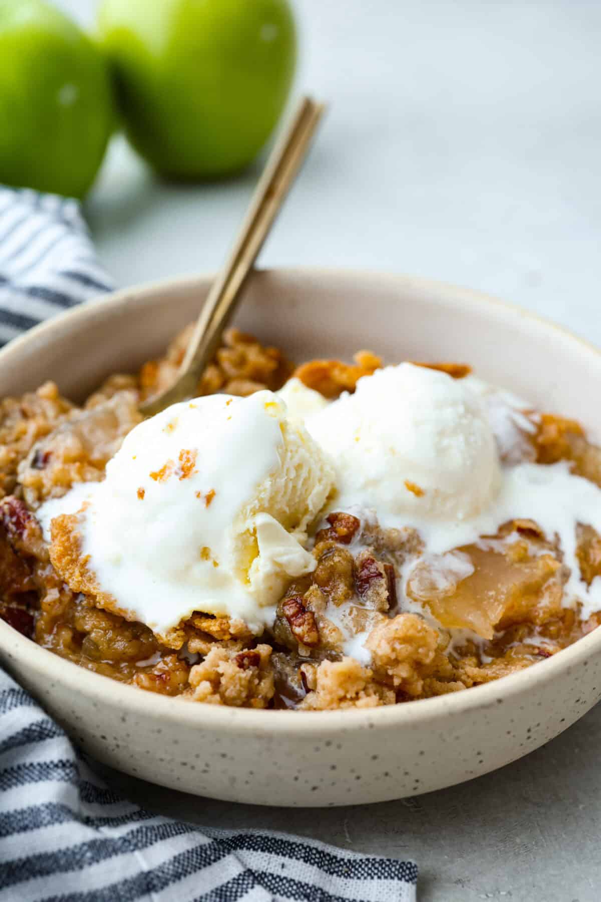 This Apple Dump Cake is your new dessert BFF. You can just toss it together, pop it in the oven, and let the magic happen. Sweet, simple, and seriously so delicious. Bowl of apple dump cake with vanilla ice cream on top.