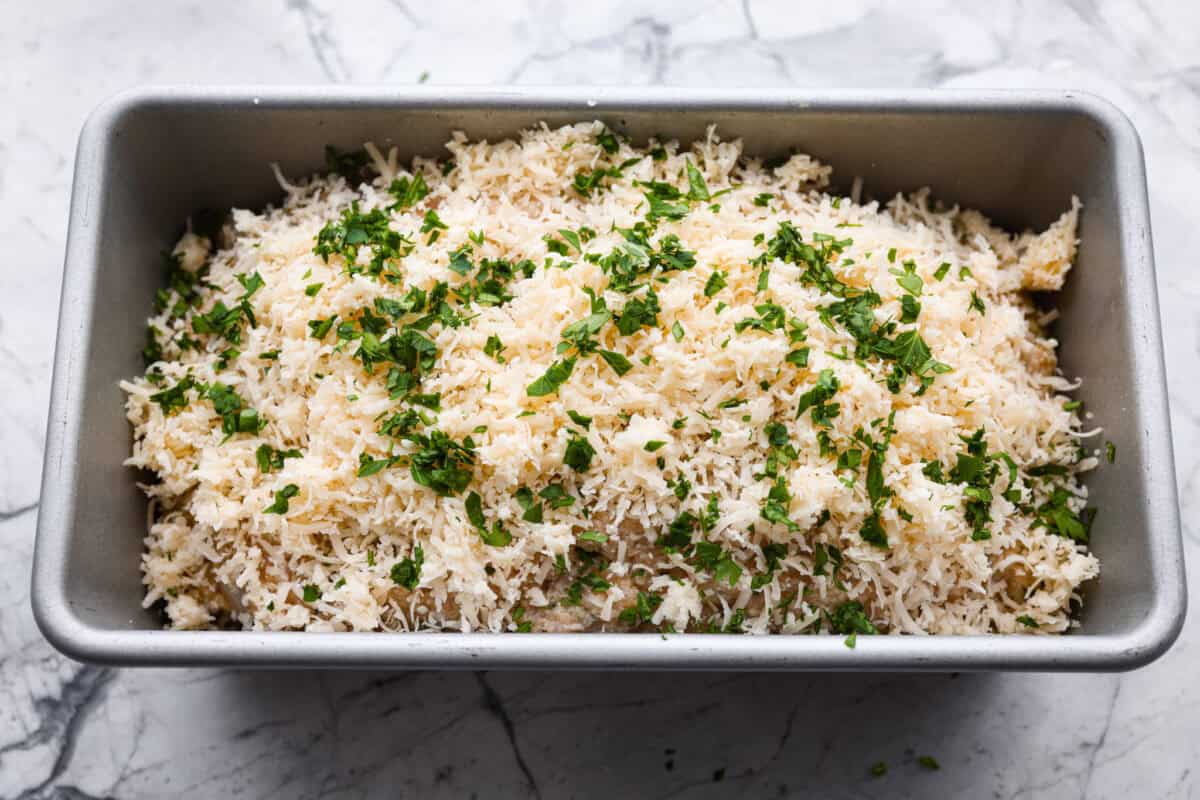 Meet your new favorite meatloaf! The ground chicken makes the Garlic Parmesan Chicken Meatloaf super moist, and you'll love the Parmesan herb-crusted topping! Parmesan and fresh parsley on top of the meatloaf ready to go in the oven.