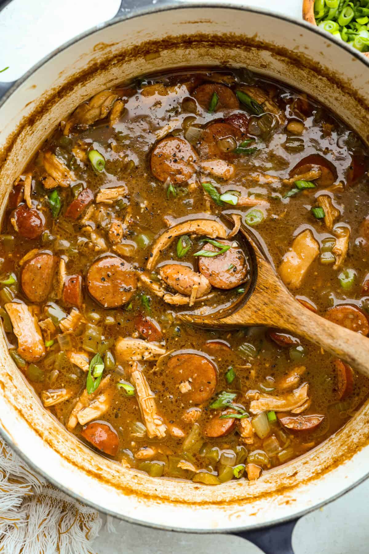 Gumbo is one of those recipes everyone makes differently, but this chicken and sausage gumbo keeps it simple. A dark roux, andouille sausage, and rotisserie chicken give you big flavor with minimal effort. Large pot of chicken and sausage gumbo with a wooden spoon.