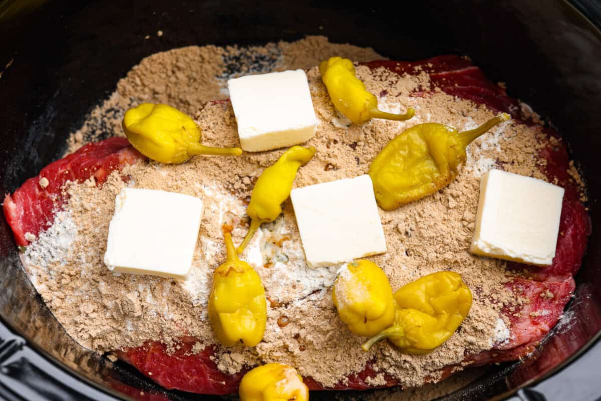 This Mississippi pot roast is melt-in-your-mouth tender, full of rich flavor, and couldnโt be easier. Just five ingredients and your slow cooker does all the work! It's a Sunday favorite at our house, and I know you'll love it too! Chuck roast covered in the seasoning packets, butter, and peppers.