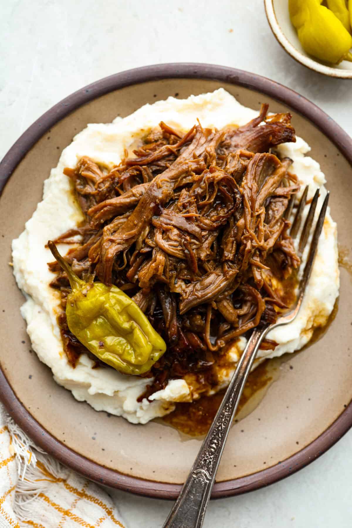 This Mississippi pot roast is melt-in-your-mouth tender, full of rich flavor, and couldnโt be easier. Just five ingredients and your slow cooker does all the work! It's a Sunday favorite at our house, and I know you'll love it too! Plated Mississippi pot roast on mashed potatoes.