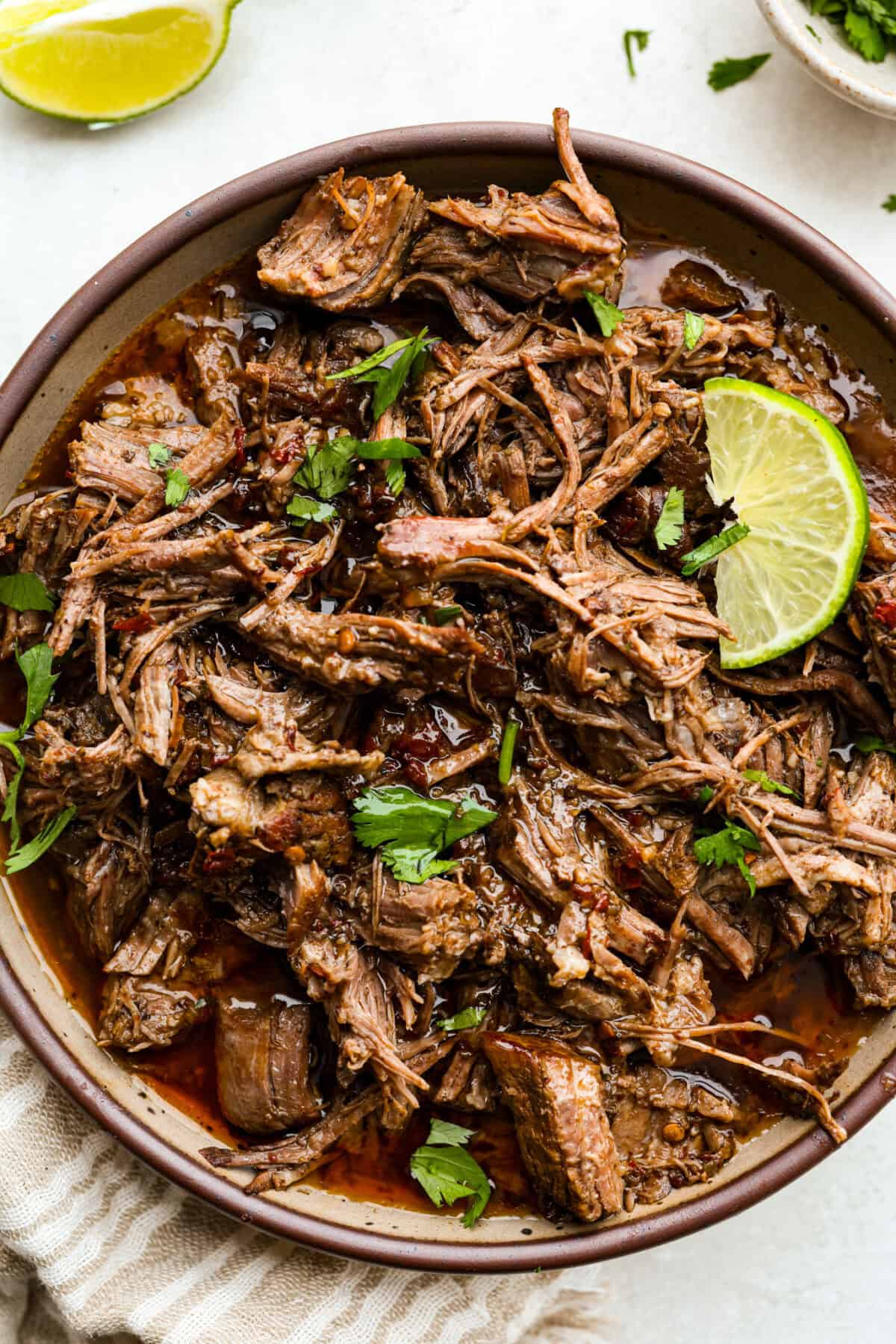 Slow cooker barbacoa beef simmers all day in smoky chipotle, tangy lime, and warm spices until it falls apart. Itโs perfect for tacos, burritos, bowls, or nachos, all with that taquerรญa-style flavor at home. Bowl of slow cooker Barbacoa beef garnished with cilantro and lime.