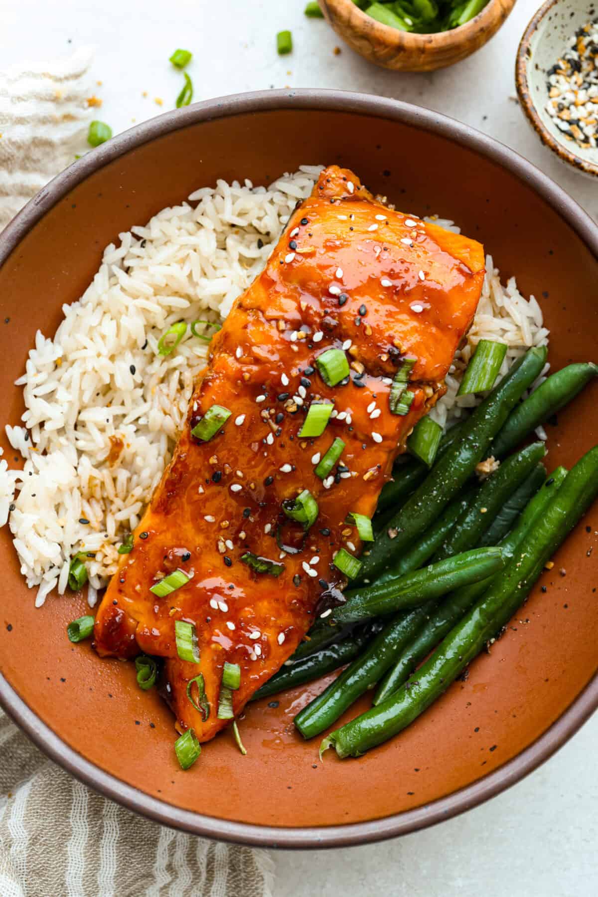 Air fryer teriyaki salmon is the best fast and tasty meal! The salmon cooks up perfectly tender with crisp edges, then gets coated in a glossy, sweet-and-savory teriyaki glaze that I know you'll love! Plated air fryer teriyaki salmon filet on a bed of white rice and a side of green beans.