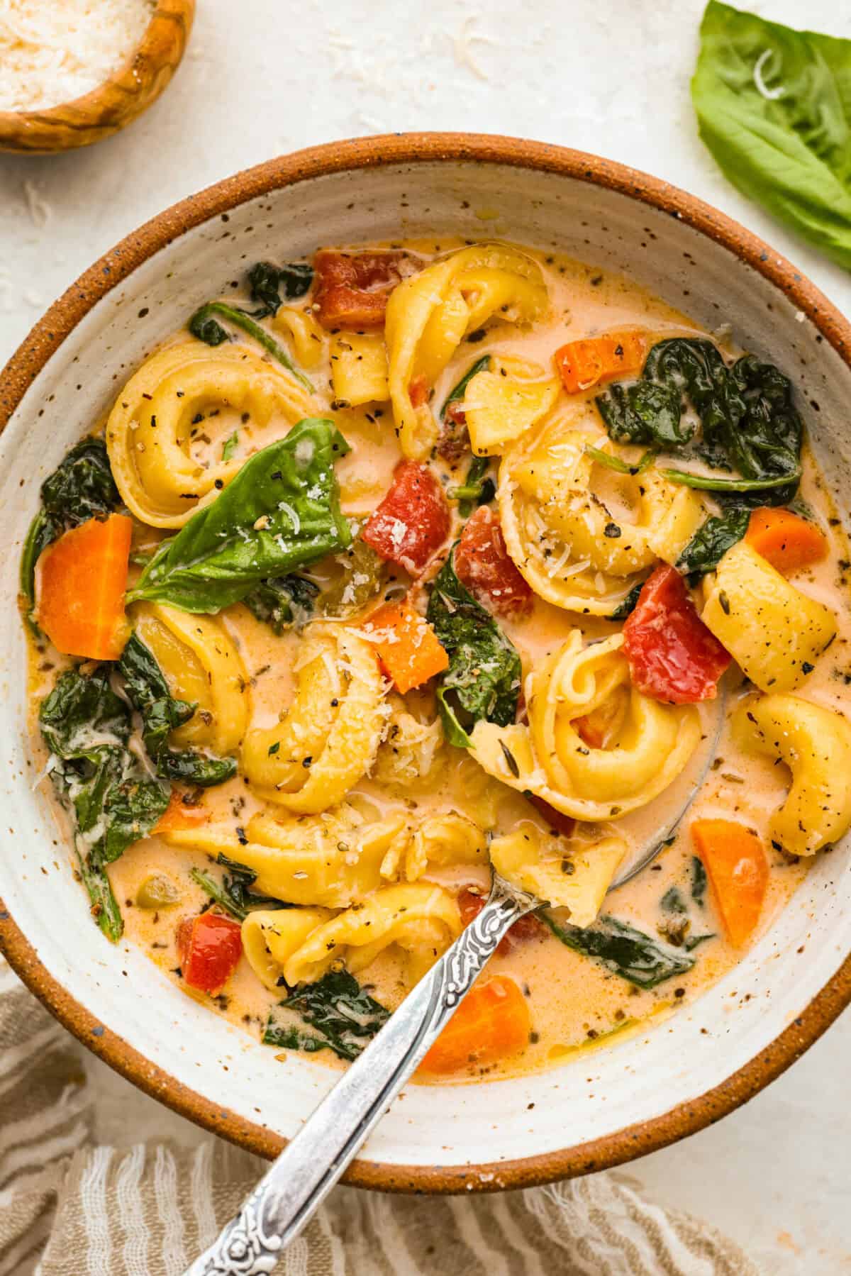 My love of cozy soups kicks in the second summer fades. This creamy tortellini soup gives me all the fall vibes. Fresh veggies, cheesy pasta, and a creamy broth, it's comfort in a bowl. Youโve got to try it today! Bowl of creamy vegetable tortellini soup.