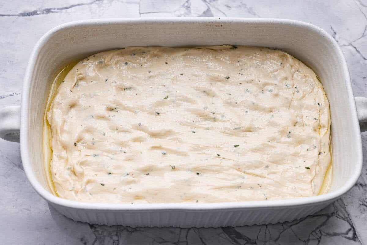 Golden, fluffy, and infused with fresh rosemary and olive oil, this rosemary focaccia is pure perfection! With its crisp edges, soft center, and irresistible herb aroma, it’s the kind of bread that disappears straight off the pan. Focaccia dough spread out in a baking with olive oil.