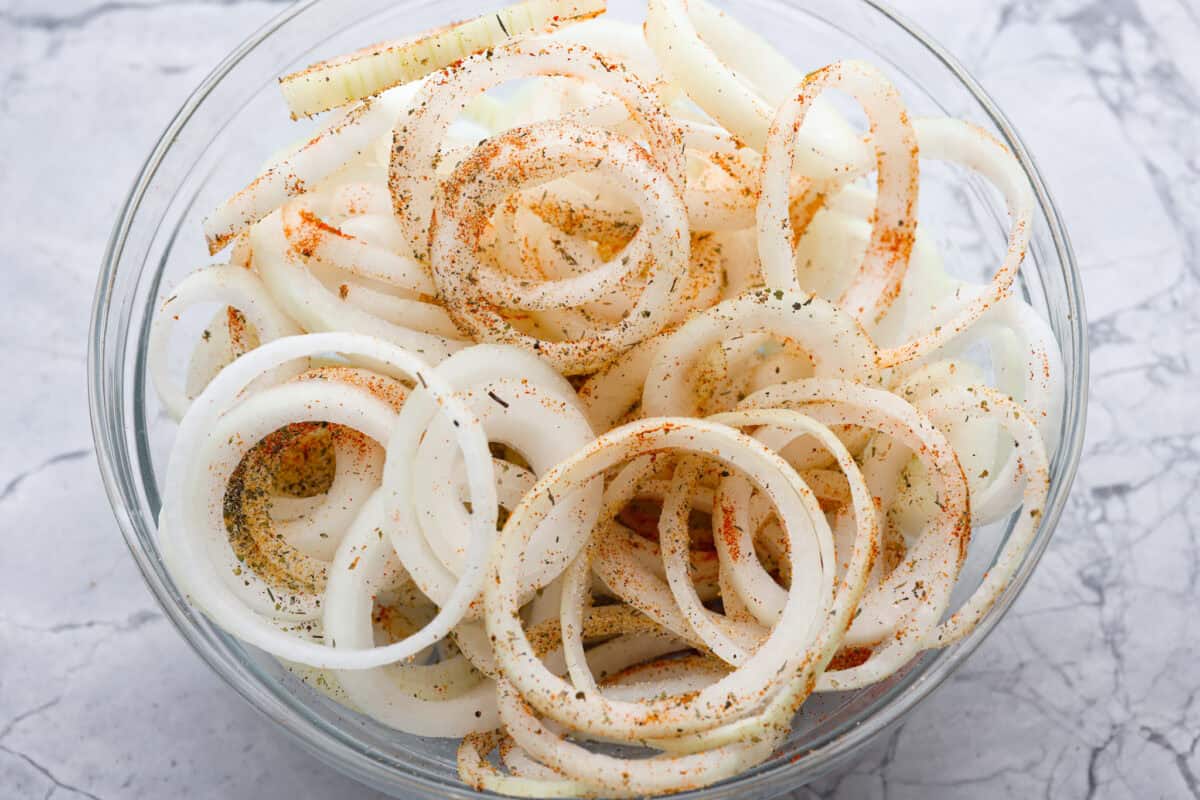 If you’ve never had Tennessee onions, bless your heart! Sweet onions bake in butter and gooey cheese until they’re golden, bubbly, and downright sinful. The perfect side to complement steak, chicken, burgers, or your favorite BBQ. Sliced onions seasoned in a bowl.