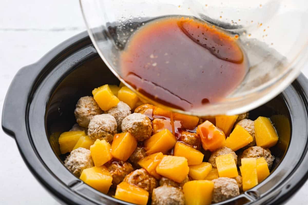 Bring the taste of the tropics to your table with Crockpot Huli Huli Meatballs! Juicy meatballs simmer in a sweet and tangy pineapple-ginger sauce, bursting with island flavor. Mixed sauce being poured over the meatballs and pineapple.