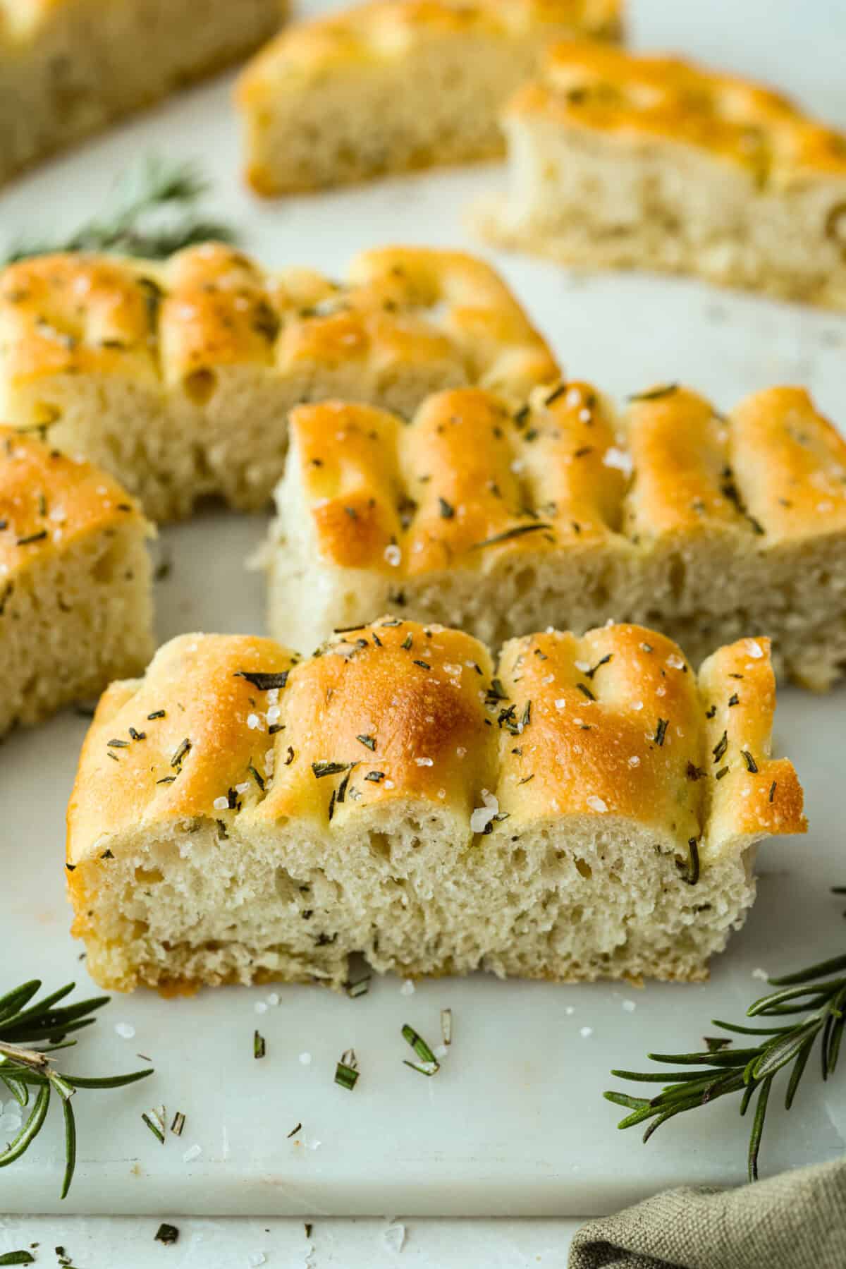Golden, fluffy, and infused with fresh rosemary and olive oil, this rosemary focaccia is pure perfection! With its crisp edges, soft center, and irresistible herb aroma, it’s the kind of bread that disappears straight off the pan. Sliced pieces of rosemary focaccia bread topped with course salt and fresh rosemary.