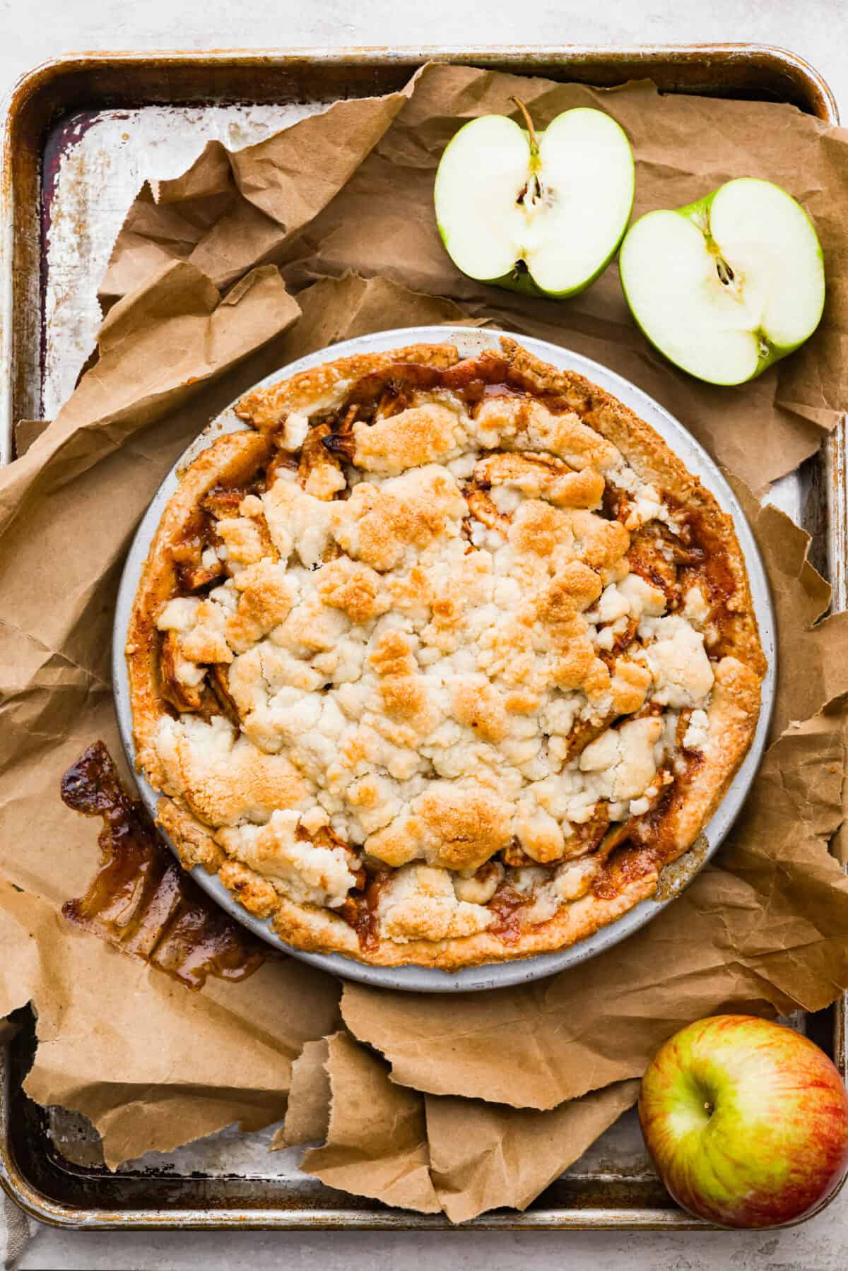 This brown bag apple pie is simple, foolproof, and downright delicious! The secret? It bakes right inside a paper bag, keeping the crust golden, the filling perfectly tender, and your oven mess-free. Overhead shot of baked brown bag apple pie on a cookie sheet with a green apple cut in half.