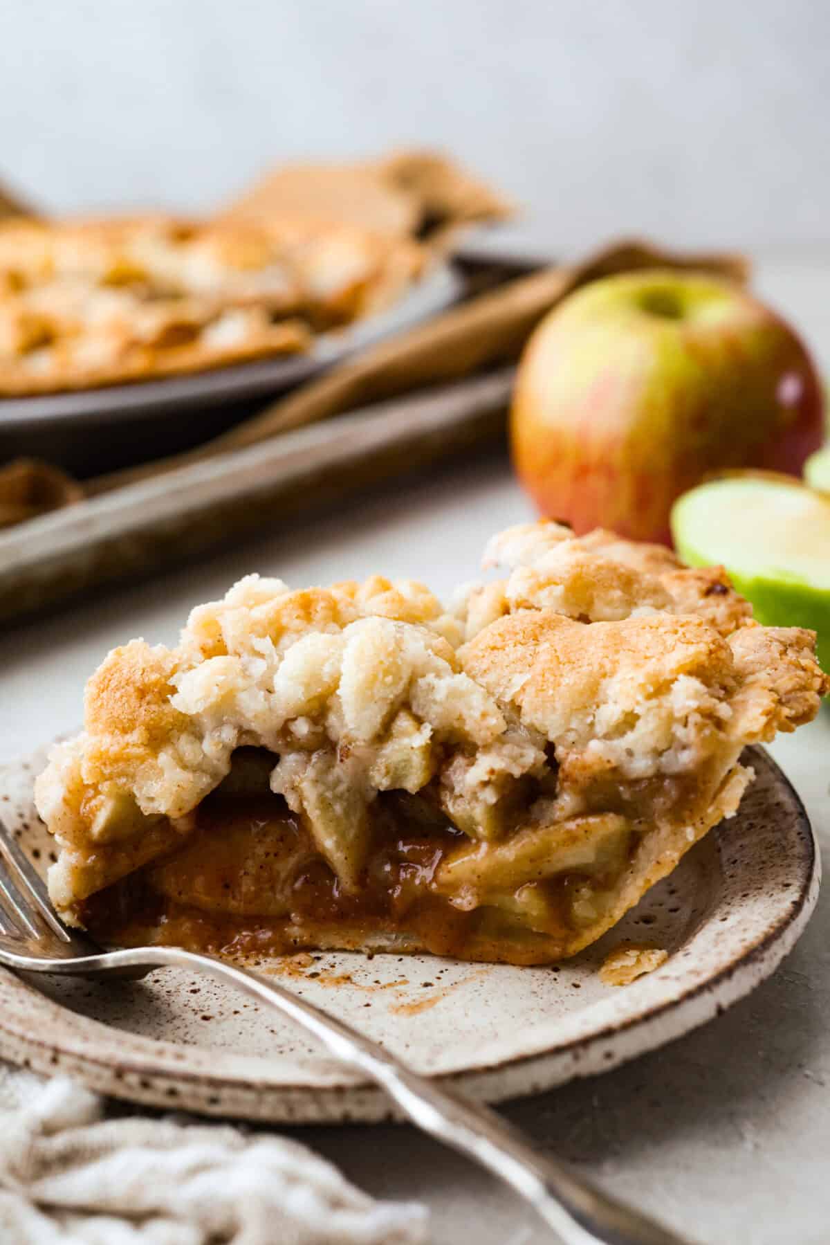 This brown bag apple pie is simple, foolproof, and downright delicious! The secret? It bakes right inside a paper bag, keeping the crust golden, the filling perfectly tender, and your oven mess-free. Slice of brown bag apple pie on a plate with a fork and apples in the background.