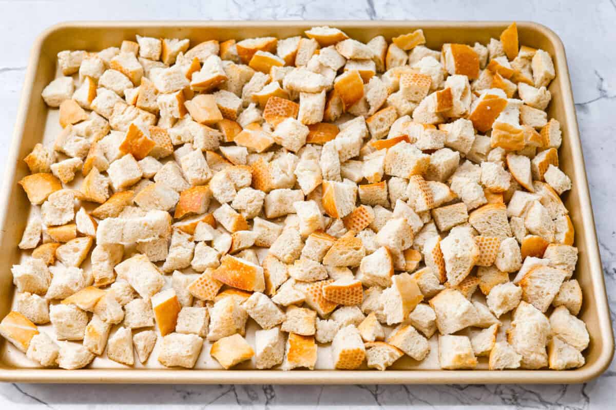 Why did it take me this long to use it in stuffing? Sourdough Stuffing's tangy crustย and the chewy middleย are perfection! Every bite soaks up all that buttery, herby goodness like it was made for this. Cubed sourdough bread on a cookie tray.