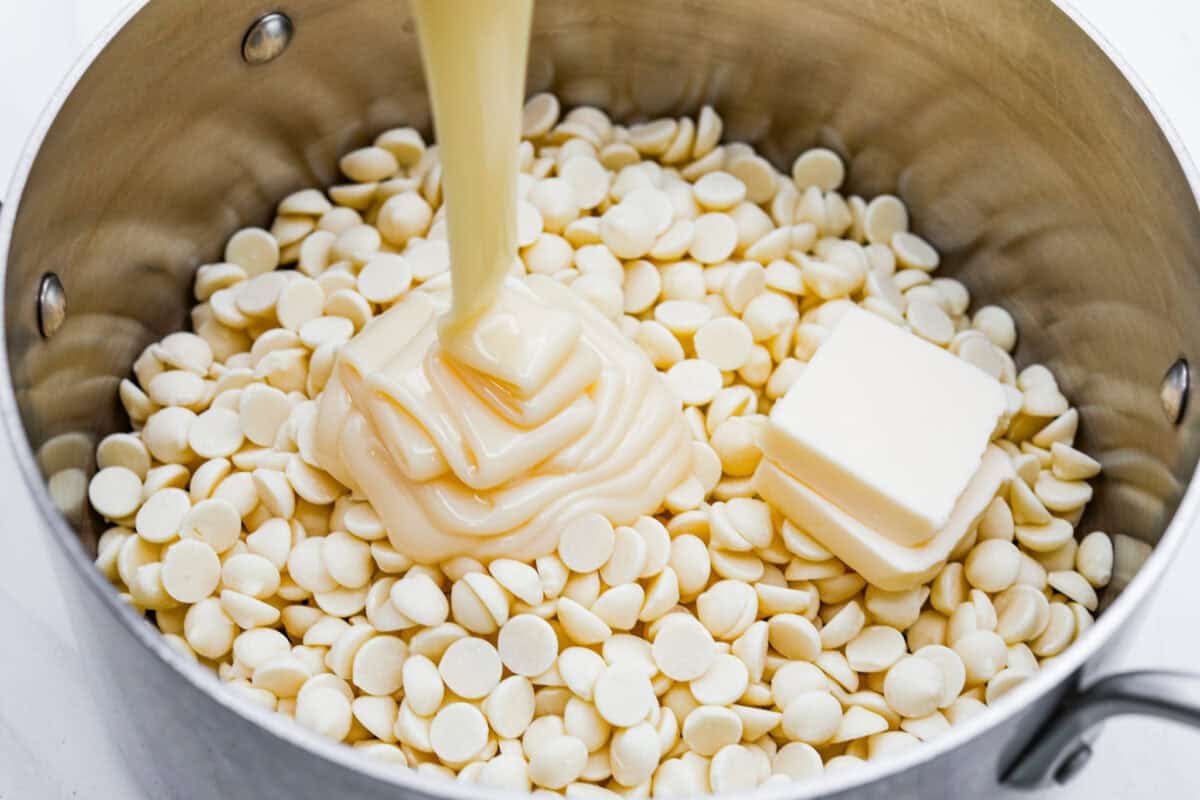 This 4-ingredient churro fudge is pure magic! It's buttery, cinnamon sugary bliss that tastes like a churro and fudge had a baby. Itโs easy to make and even easier to gift (if you can resist eating it all first!). Someone pouring sweetened condensed milk into a sauce pan with white chocolate and butter.