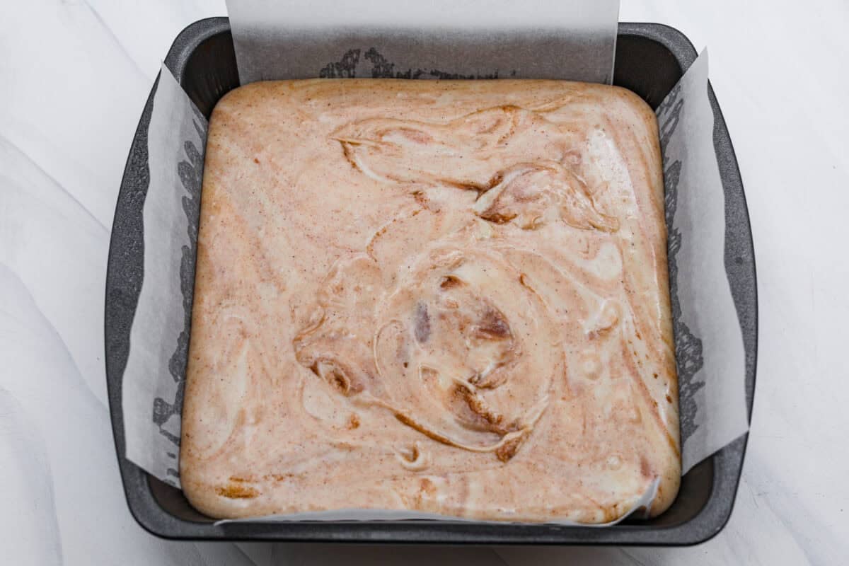This 4-ingredient churro fudge is pure magic! It's buttery, cinnamon sugary bliss that tastes like a churro and fudge had a baby. Itโs easy to make and even easier to gift (if you can resist eating it all first!). Overhead shot of the fudge mixture poured into a 8x8 pan with parchment paper.