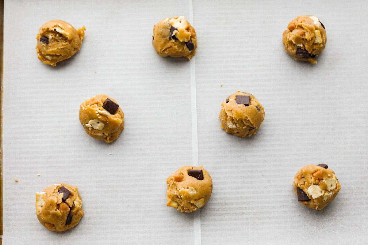 Skip the candy making! These Christmas Crack Cookies give you all the buttery, chocolatey, toffee filled flavor of Christmas crack in one easy cookie recipe. Gooey, salty, and completely irresistible. Christmas crack cookie dough balls spread evenly on a cookie sheet.