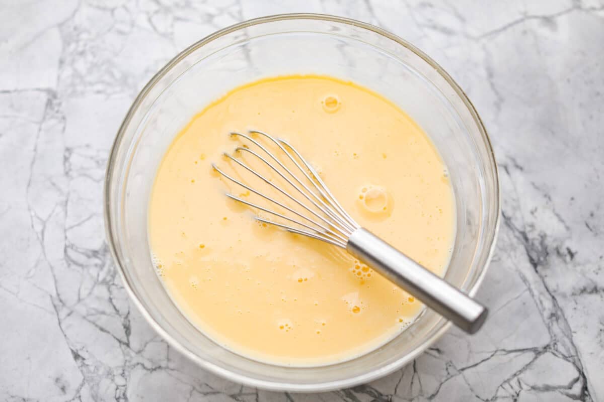Wake up to a breakfast that feels like a warm hug! This Christmas morning casserole turns sausage, eggs, cheese, and fluffy biscuits into the easiest, hearty breakfast you can't get enough of! Eggs and milk whisked together in a mixing bowl.
