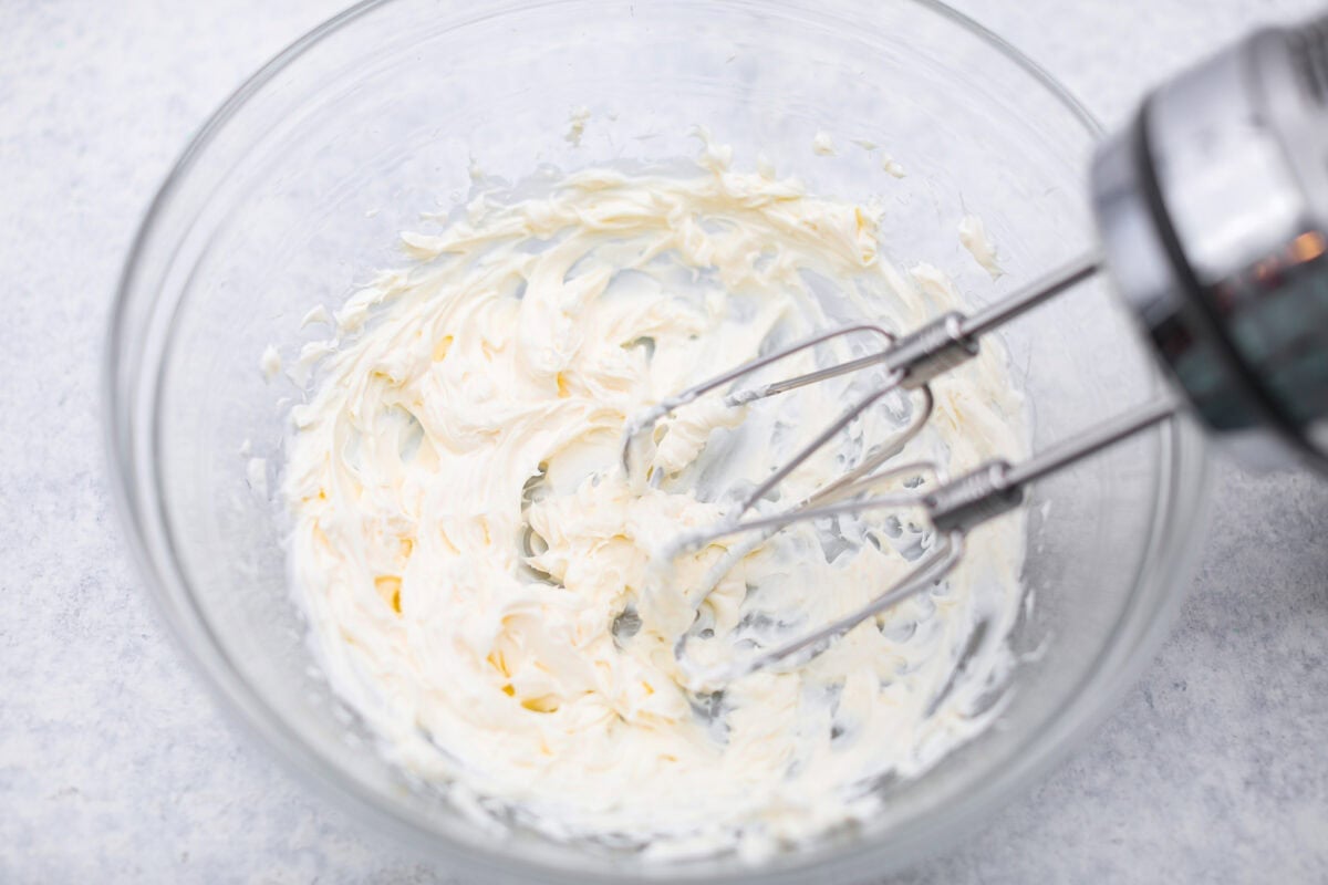 This Christmas ribbon salad brings all the festive vibes with its bright, sliceable layers. It looks fancy, but the process is super easy and mostly hands-off. Make it ahead and watch it disappear! Cream cheese being beaten with a hand mixer in a mixing bowl.