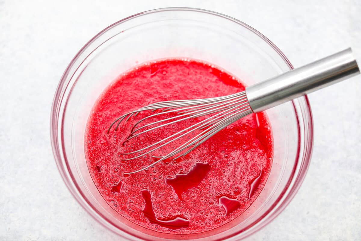 This Christmas ribbon salad brings all the festive vibes with its bright, sliceable layers. It looks fancy, but the process is super easy and mostly hands-off. Make it ahead and watch it disappear! Raspberry Jello being whisked together.