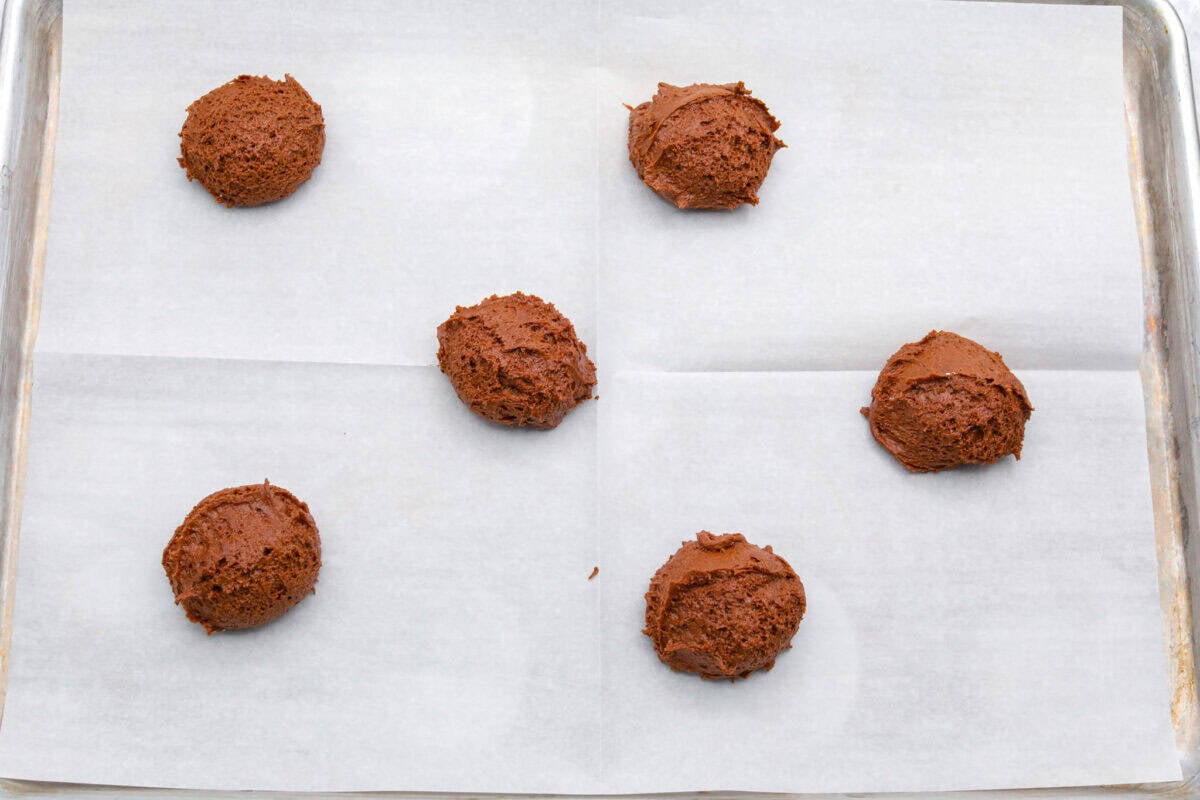 Hostess Cupcake Cookies are soft chocolate cookies filled with sweet marshmallow and topped with smooth chocolate ganache. They’re rich, fun, and always a hit. Balls of cookie dough added to a cookie sheet with parchment paper.