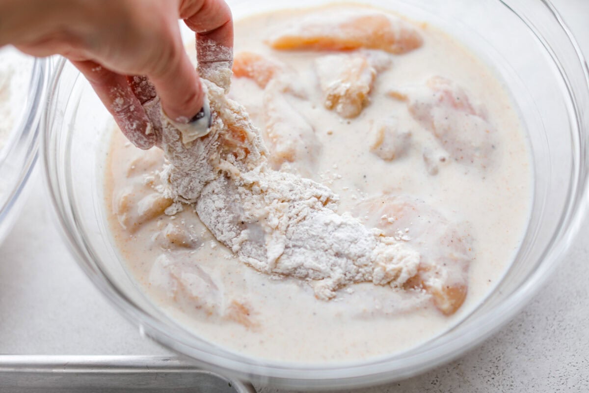 Make this copycat Raising Cane’s chicken tenders at home, no drive-thru required. An easy marinade, simple ingredients, and a quick fry give you crisp, light chicken and that unmistakable Cane’s sauce for a fraction of the cost. Breaded chicken tender being dipped back into the marinade for a second coating.