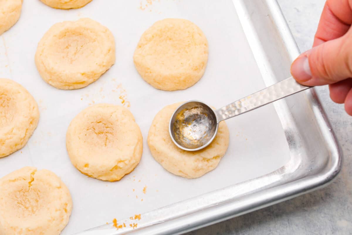 Meet the upgraded Twix thumbprint cookies! I reโtested and updated the recipe so you'll get defined wells, clean edges, and a tender center every time! They are perfect for gift giving and cookie parties! Someone pressing the teaspoon into the baked cookies.