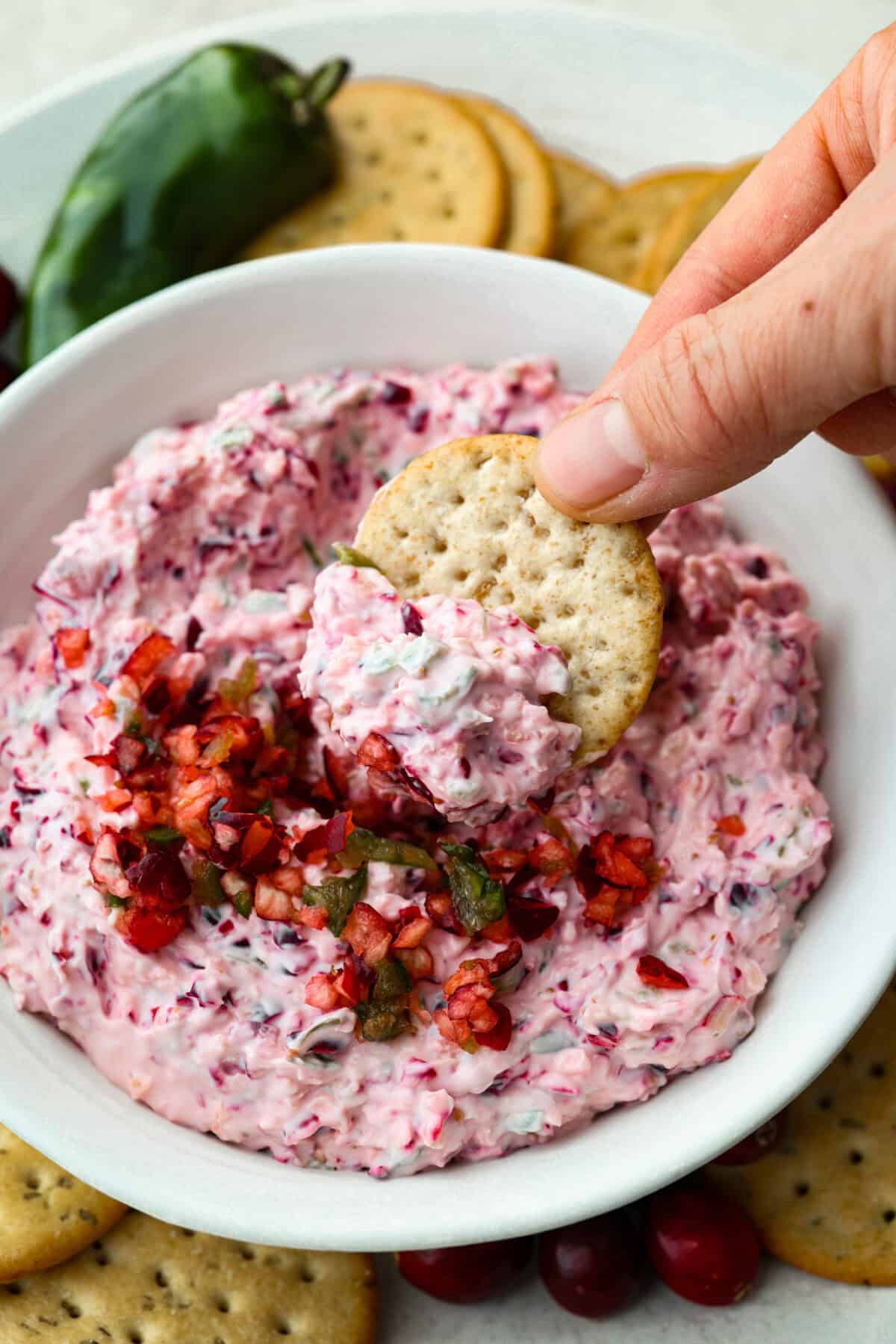 This cranberry jalapeño dip is my fresh take on the cult favorite Costco version. It's bright, tangy, a little spicy, and wildly easy to make at home. It’s the same addictive flavor, but you get to make it how you like! Someone scooping a bite of the cranberry jalapeño dip with a cracker.