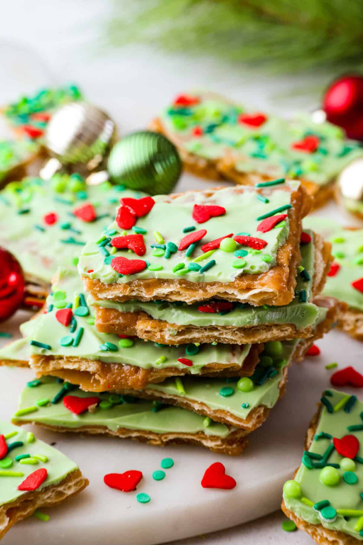 If you want a quick, crunchy treat with a bit of holiday mischief, this Grinch Christmas Crack is it. Sweet, salty, and totally addictive. My classic Christmas Crack is always a hit, but this version brings all the Grinchy fun! Stack Grinch Christmas crack in fornt of some Christmas bobbles.
