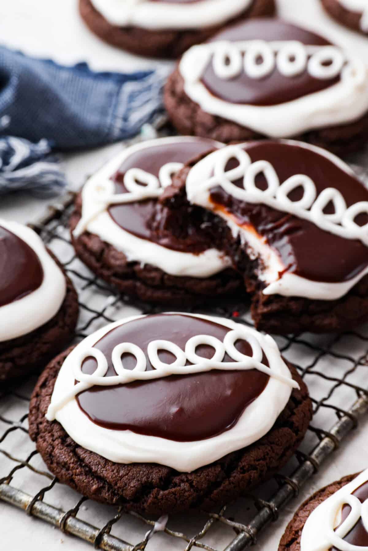 Hostess Cupcake Cookies are soft chocolate cookies filled with sweet marshmallow and topped with smooth chocolate ganache. They’re rich, fun, and always a hit. Close up shot of Hostess Cupcake cookies on a wire rack, with one missing a bite.