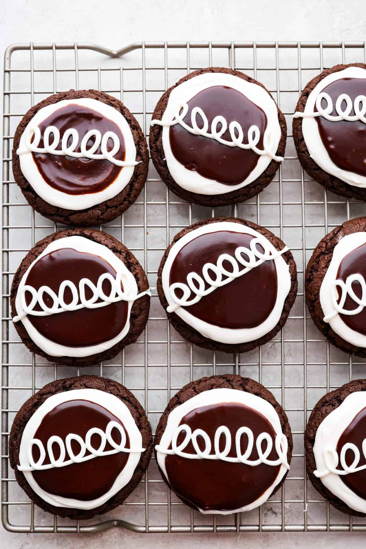 These Hostess Cupcake Cookies take your favorite childhood treat and turn it into soft, chocolate cookies! They are topped with sweet marshmallow and smooth chocolate ganache, and of course, the classic white swirl! Overhead shot of Hostess Cupcake cookies completed and spread out on a cooling rack.