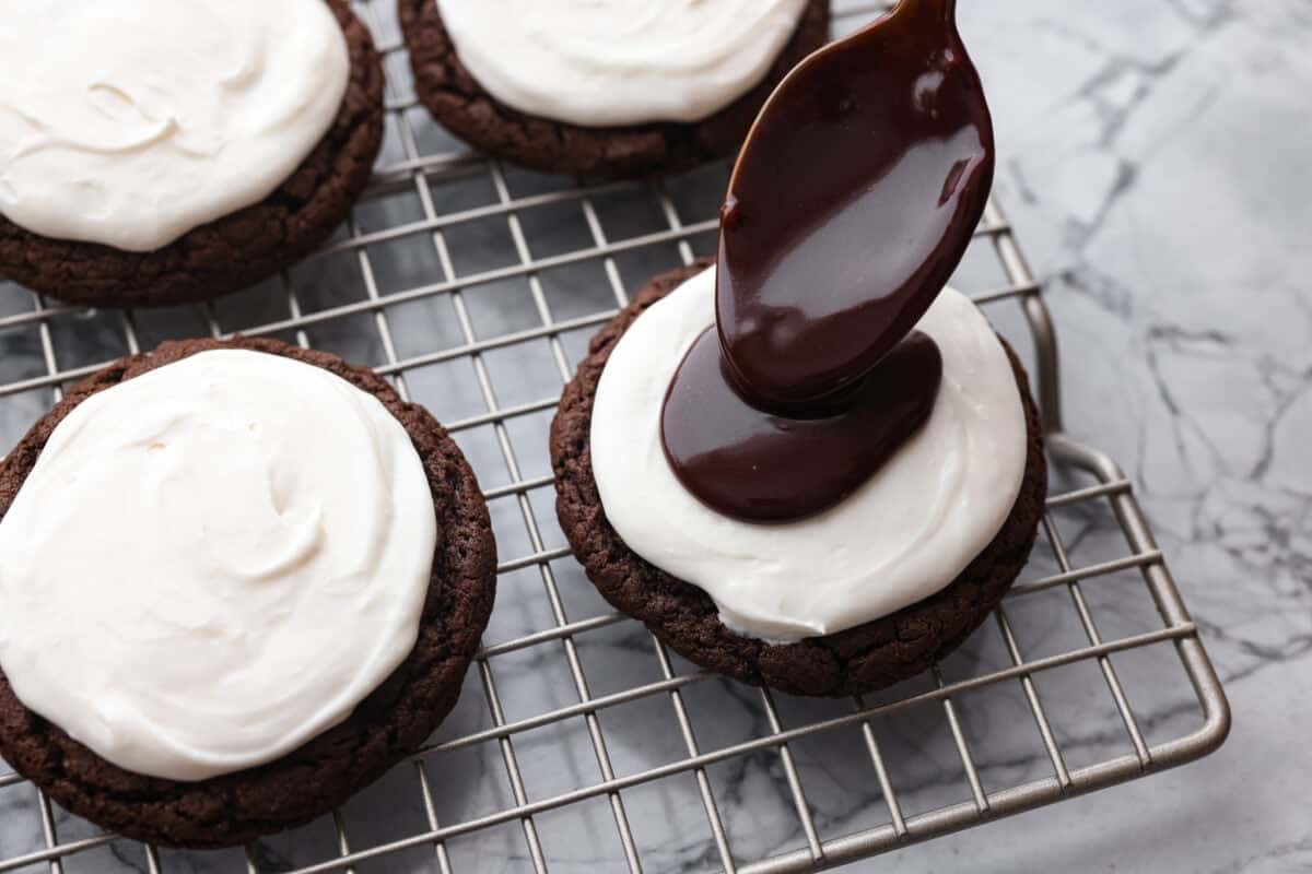 These Hostess Cupcake Cookies take your favorite childhood treat and turn it into soft, chocolate cookies! They are topped with sweet marshmallow and smooth chocolate ganache, and of course, the classic white swirl! Someone spooning on a dollop of chocolate ganache.