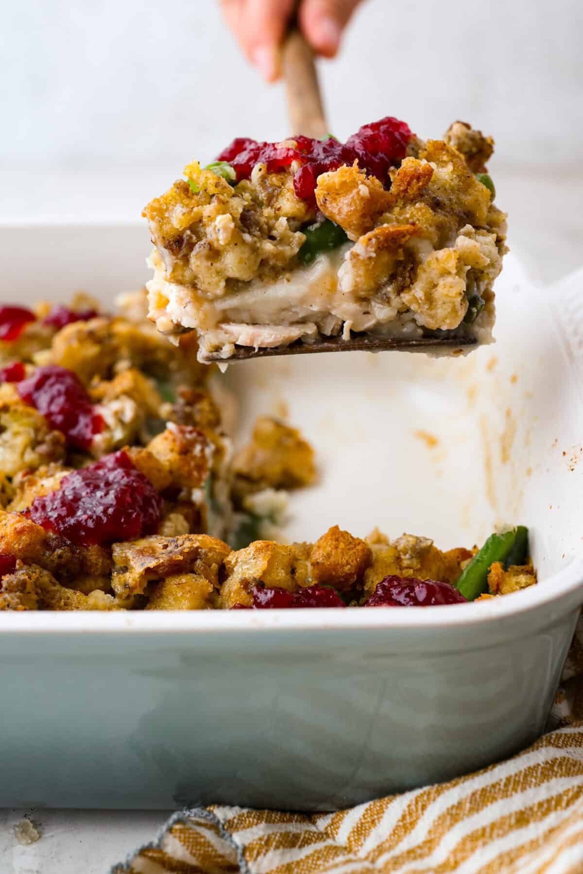 This Thanksgiving leftover casserole is the best way to enjoy every last bit of your holiday meal. I give you tips for keeping it moist, flavorful, and perfectly layered. Someone lifting a serving of Thanksgiving leftover casserole out of the baking dish.