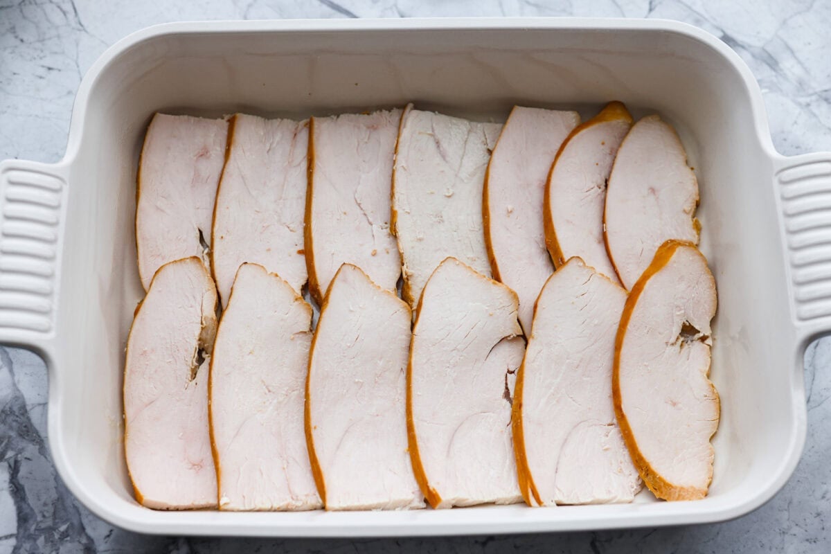 This Thanksgiving leftover casserole is the best way to enjoy every last bit of your holiday meal. I give you tips for keeping it moist, flavorful, and perfectly layered. Turkey slices layered on the bottom of a baking dish.