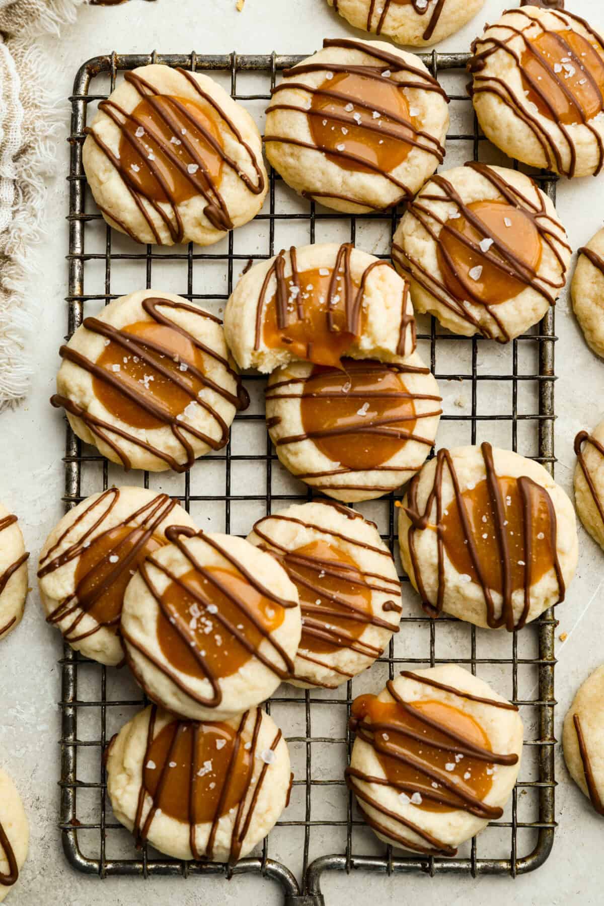 Meet the upgraded Twix thumbprint cookies! I reโtested and updated the recipe so you'll get defined wells, clean edges, and a tender center every time! They are perfect for gift giving and cookie parties! Overhead shot of Twix thumbprint cookies on a cooling rack.