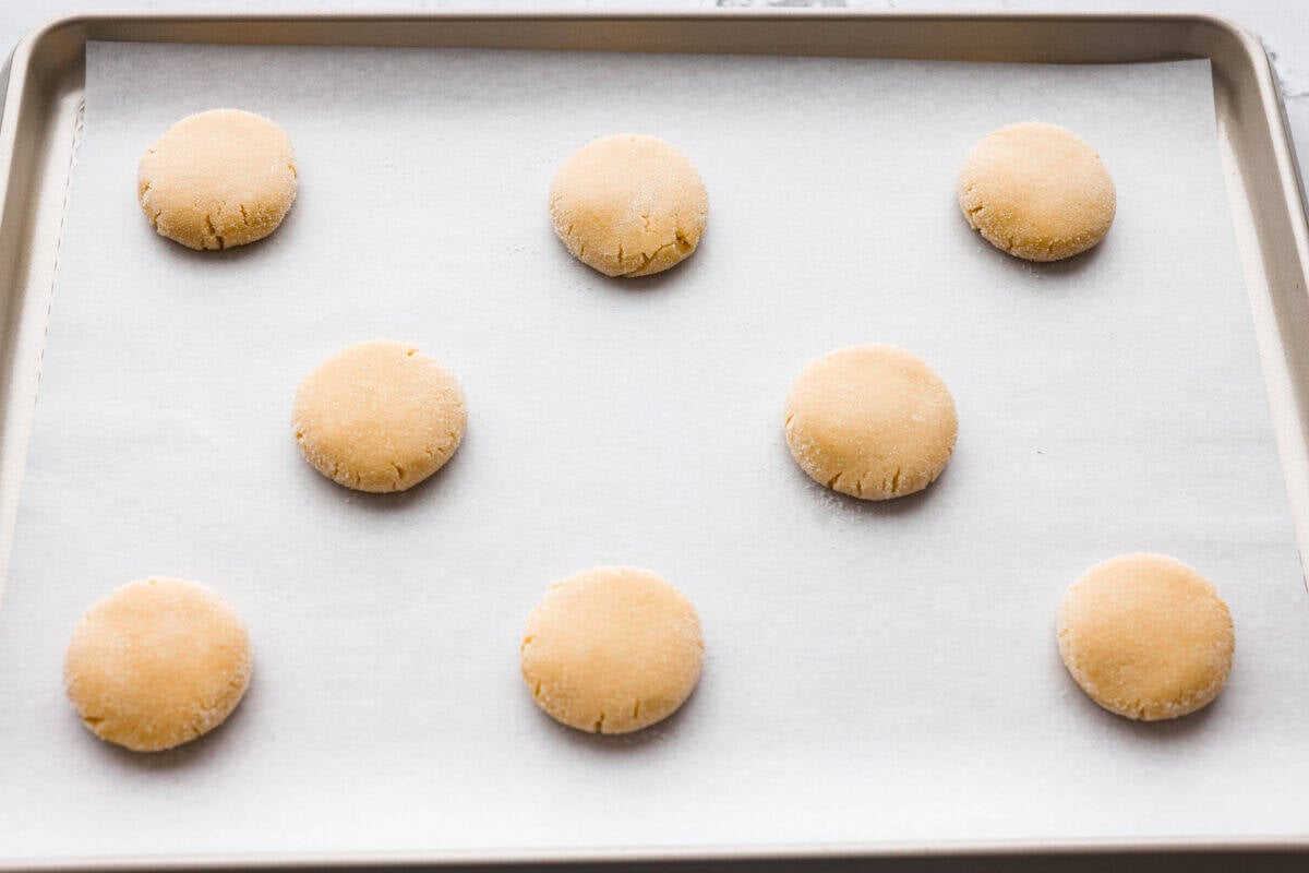 Simple to make and impossible to resist, these 4 ingredient sugar cookies are soft, tender, and sweet. A quick mix, a little roll, and your kitchen will smell like pure cookie heaven! Cookie dough balls smashed slightly.