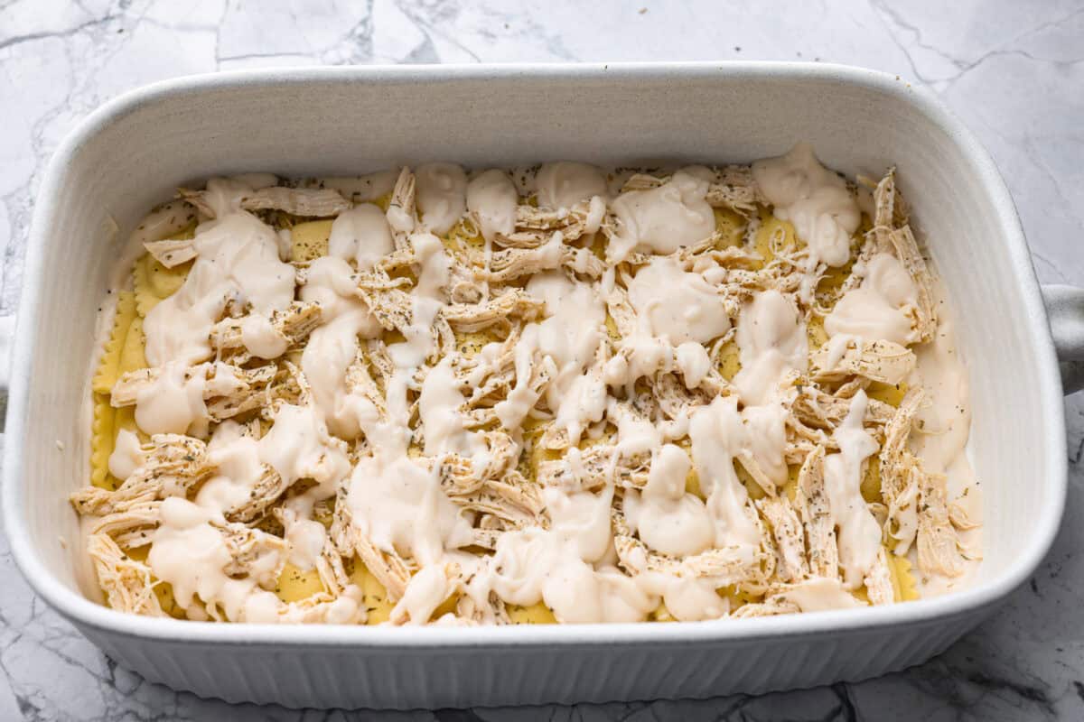 By the end of the day, Iโm wiped and still somehow expected to make dinner. I'm telling you, this Alfredo ravioli casserole will swoop in and save the day! Simply layer, bake, and enjoy! Chicken and sauce layered on top of the ravioli.