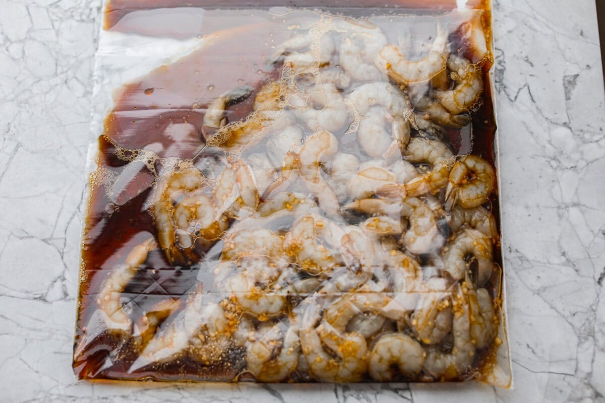 Bourbon shrimp are sticky, garlicky, and packed with flavor. Sweet brown sugar and a splash of bourbon create a quick, glossy glaze that makes this appetizer (or weeknight dinner!) totally irresistible. A ziplock bag with marinade and shrimp in side.