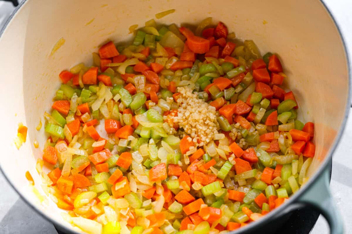 Stop what you are doing right now, and make this Crack Chicken and Rice soup! With tender chicken, rice, creamy cheese, crispy bacon, and bold ranch flavor, this easy one pot recipe tastes like pure comfort in every spoonful. Celery, carrots, and onion cooking in a pot, with garlic added to it.