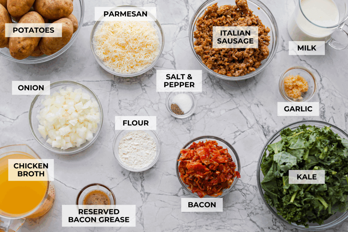 I am begging you guys to make this Zuppa Toscana Casserole! It turns the classic soup into the most delicious bake! It has layers of potatoes, sausage, bacon, kale, and cheese drenched in the most amazing sauce! Make it today, trust me! Overhead shot of labeled Zuppa Toscana casserole ingredients.