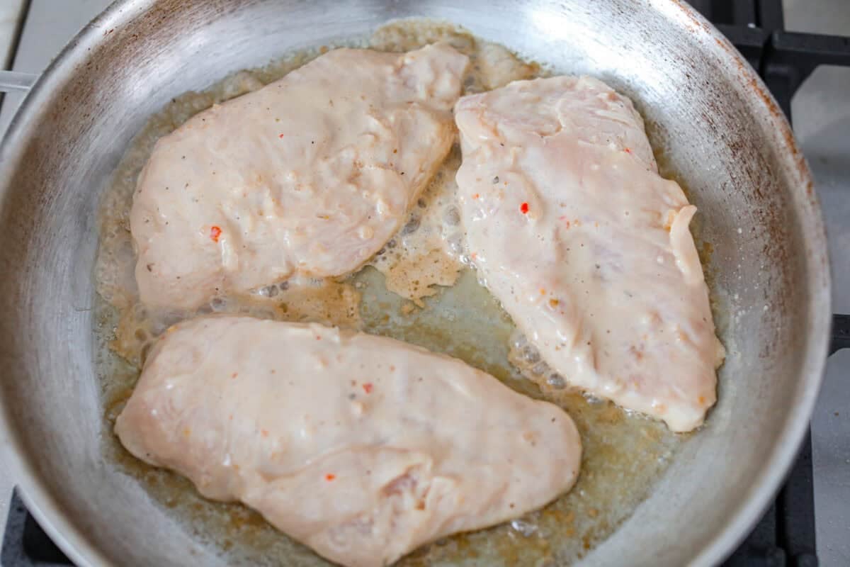 My copycat Longhorn parmesan crusted chicken brings all the cheesy, buttery goodness from the restaurant straight to your kitchen. Juicy ranch chicken is topped with a creamy cheese sauce and a golden crumb crust. Marinated chicken cooking on a hot skillet.