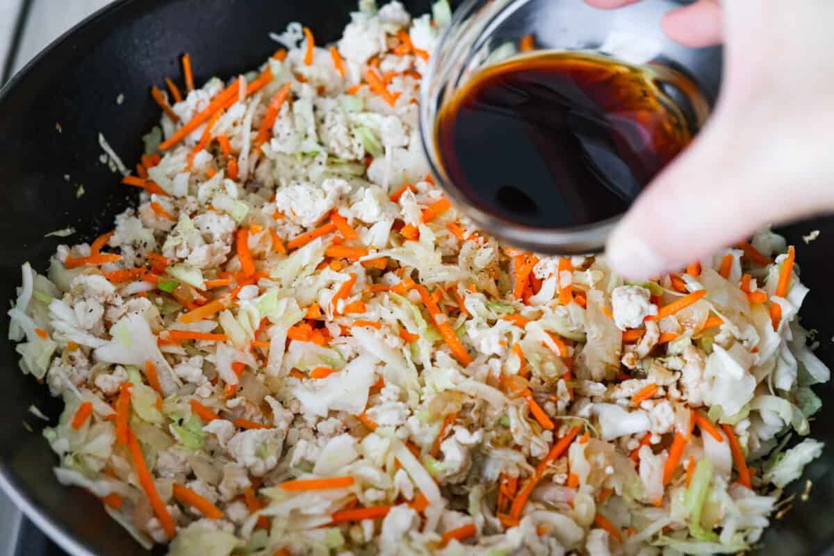 If you havenโt tried egg roll in a bowl yet, youโre in for a treat. Everything you love inside of an egg roll in a lighter, healthier, no-wrapper version! It's ready in 15 minutes, making it a perfect weeknight meal! Soy sauce being poured over the coleslaw and turkey mixture.