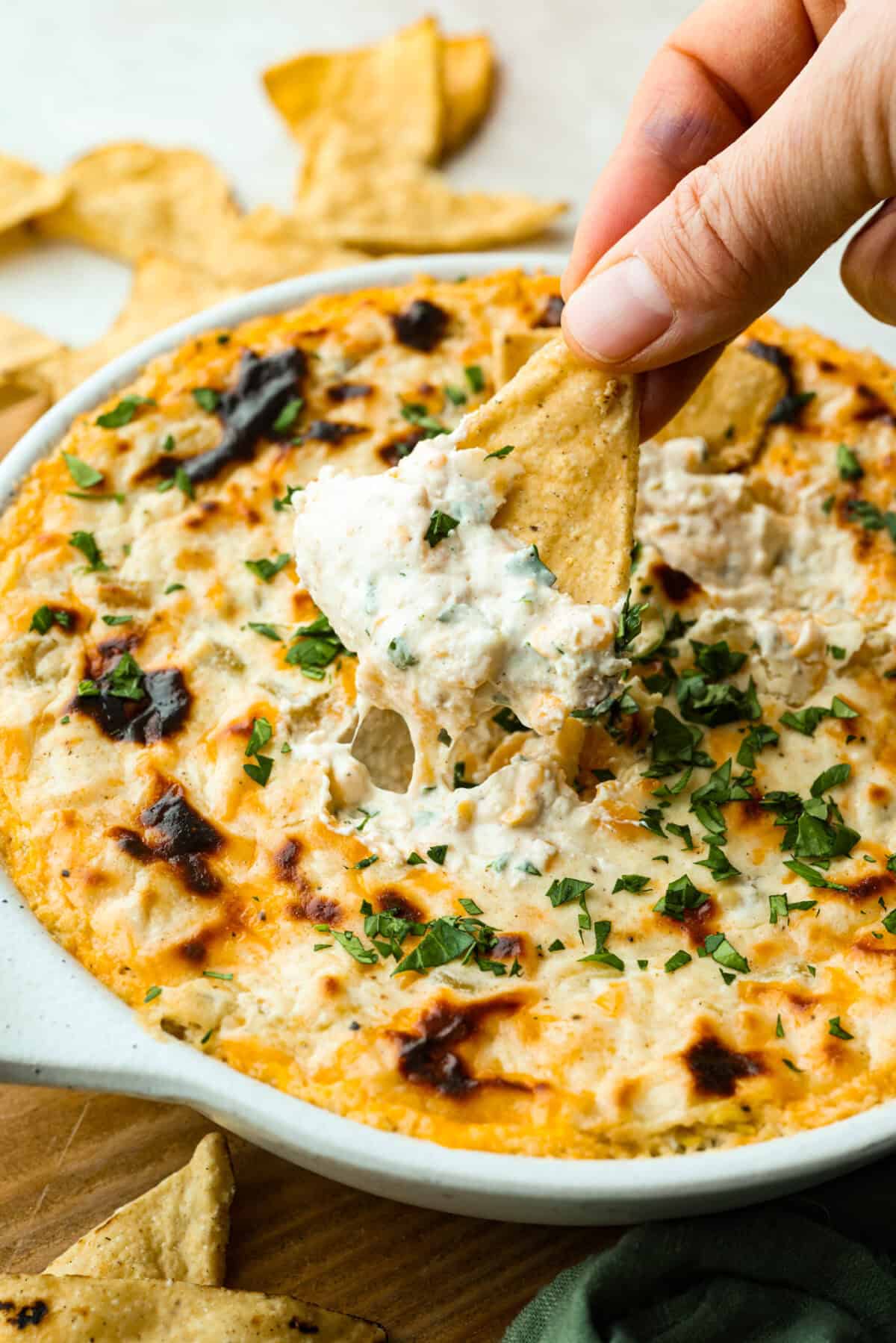 Someone scooping a bit of green chile dip onto a chip.
