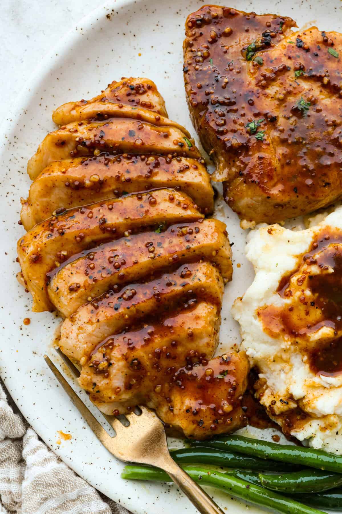 These honey mustard pork chops bring big flavor with very little effort. The whole grain mustard adds texture and bite, while a few extra spices deepen the sauce, turning a simple skillet dinner into something totally crave-worthy. Plated honey mustard pork chops next to mashed potatoes and green beans.