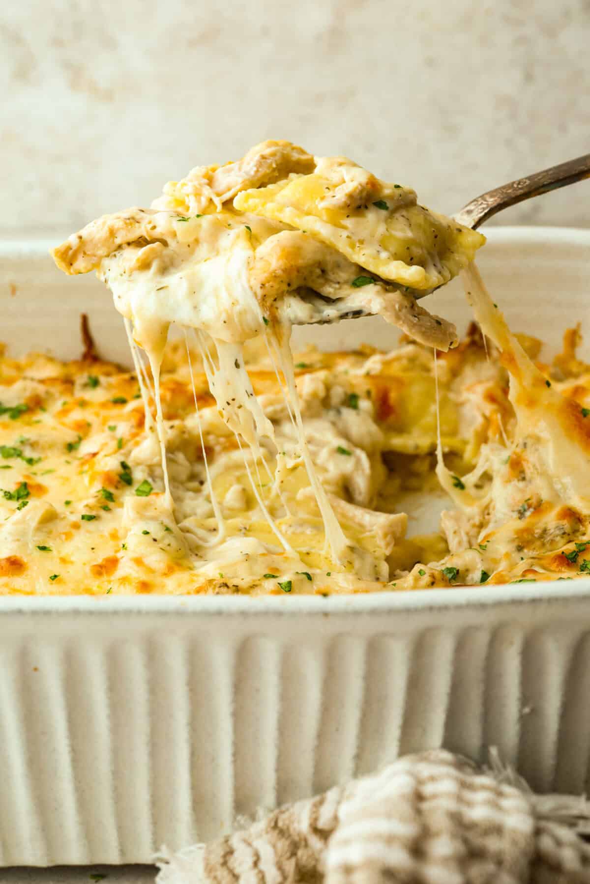By the end of the day, Iโm wiped and still somehow expected to make dinner. I'm telling you, this Alfredo ravioli casserole will swoop in and save the day! Simply layer, bake, and enjoy! Someone scooping a portion of alfredo ravioli casserole from the baking dish.