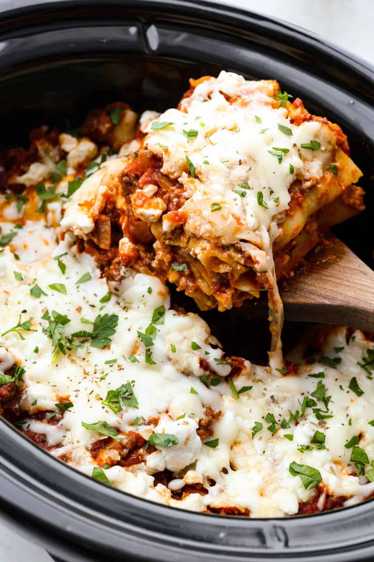 This easy slow cooker lasagna layers tender noodles with rich meat sauce and three cheeses, all with just 25 minutes of hands on prep. You get classic, cozy lasagna flavor that melds into every bite from slow cooking all day! Someone pulling a scoop of slow cooker lasagna out of the crockpot.