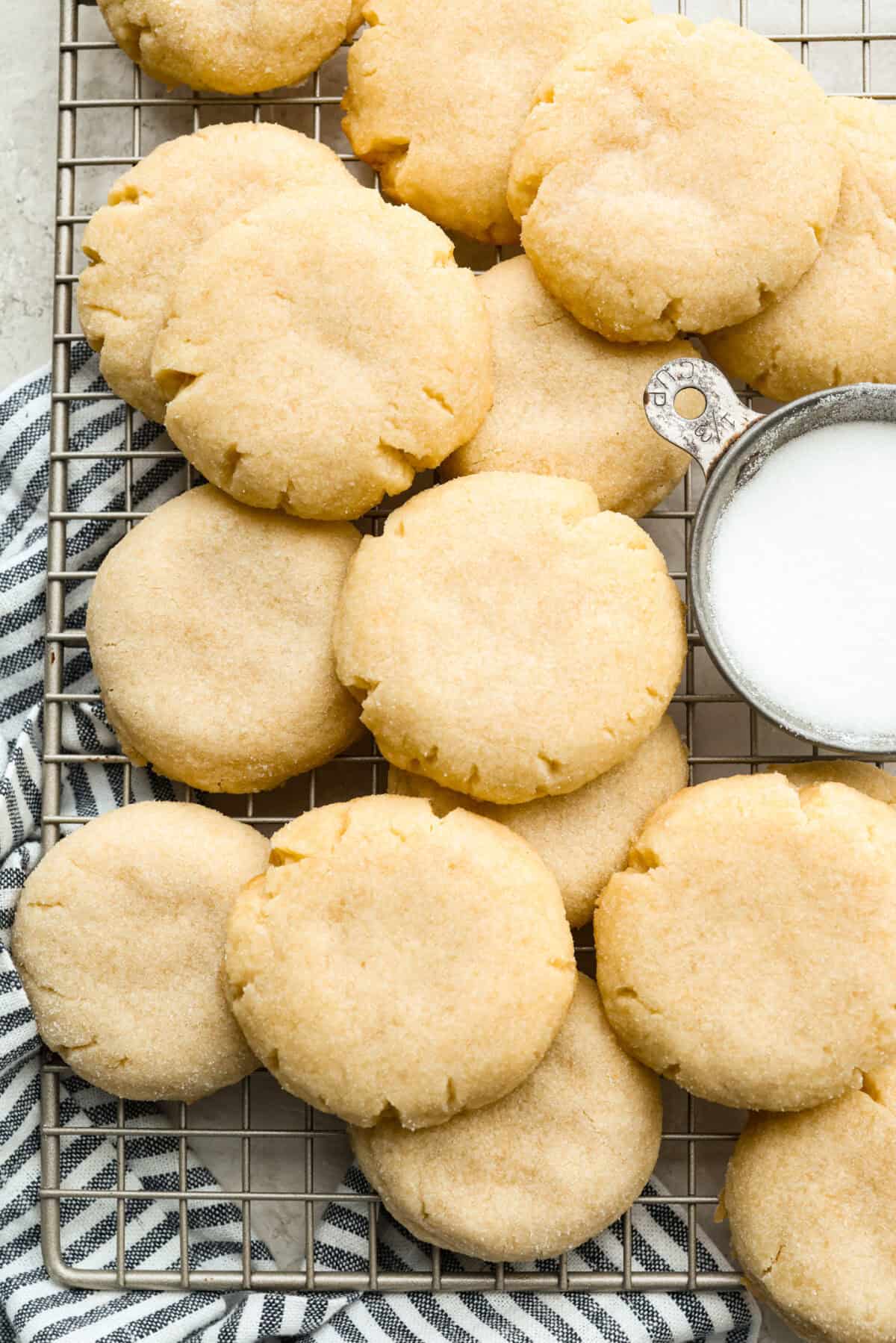 Simple to make and impossible to resist, these 4 ingredient sugar cookies are soft, tender, and sweet. A quick mix, a little roll, and your kitchen will smell like pure cookie heaven! 4 ingredient sugar cookies layered on a cooling rack.