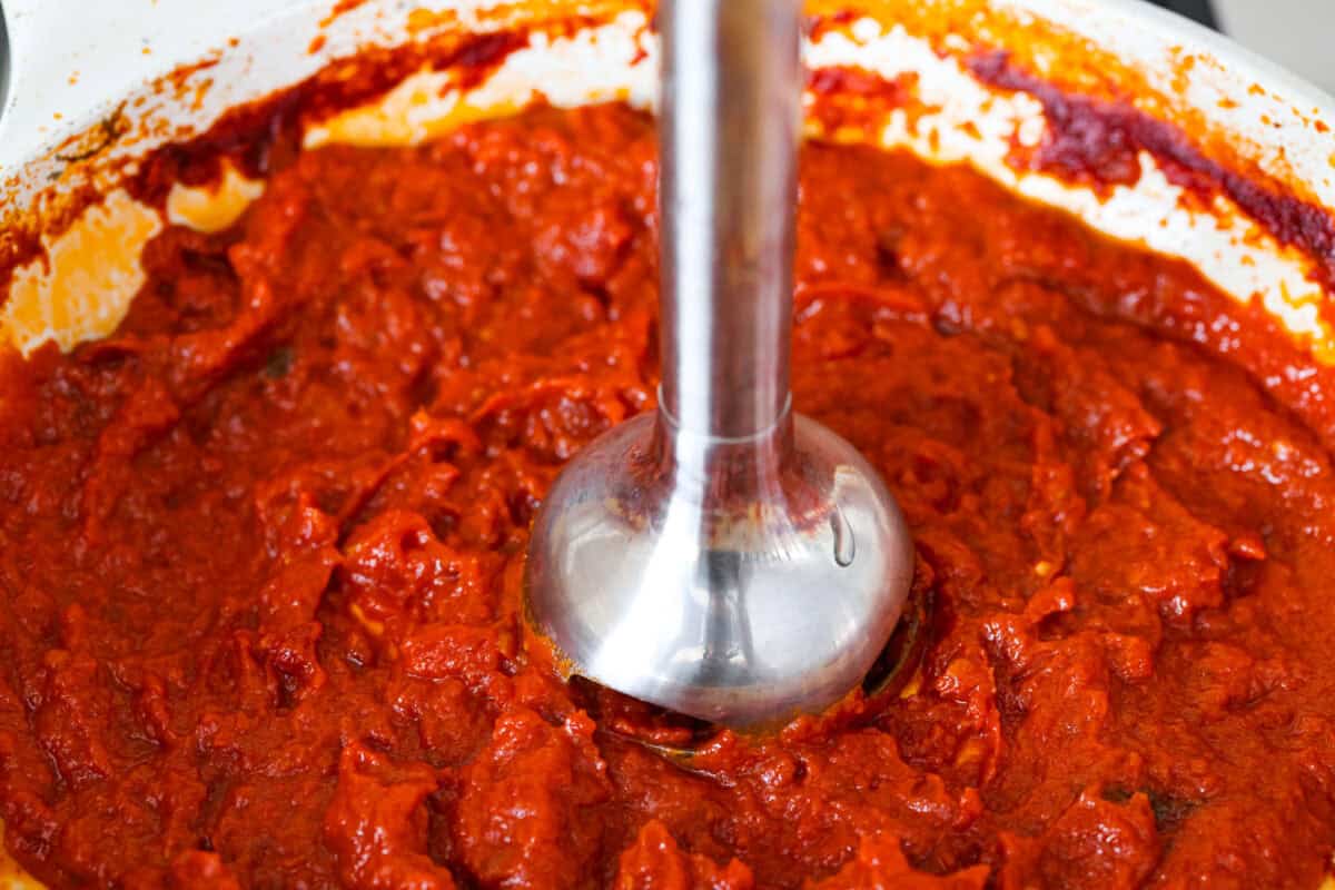 Simple, classic, and downright magical, this iconic Marcella Hazan's tomato sauce uses only 3 ingredients and proves that less is more. With just tomatoes, butter, and onion, it turns pantry staples into a rich, silky sauce you’ll make on repeat. Someone using an emersion blender to blend up the sauce.