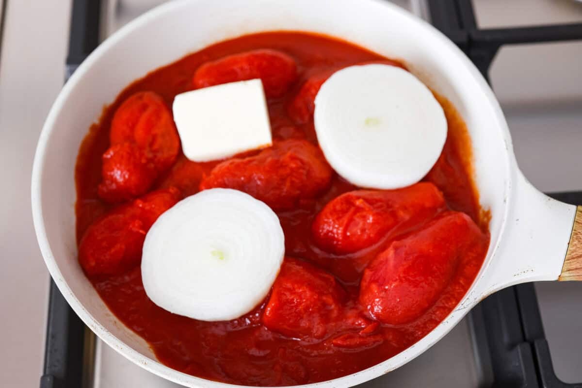 Simple, classic, and downright magical, this iconic Marcella Hazan's tomato sauce uses only 3 ingredients and proves that less is more. With just tomatoes, butter, and onion, it turns pantry staples into a rich, silky sauce you’ll make on repeat. Tomatoes, onions, and nutter in a sauce pan on the stove.