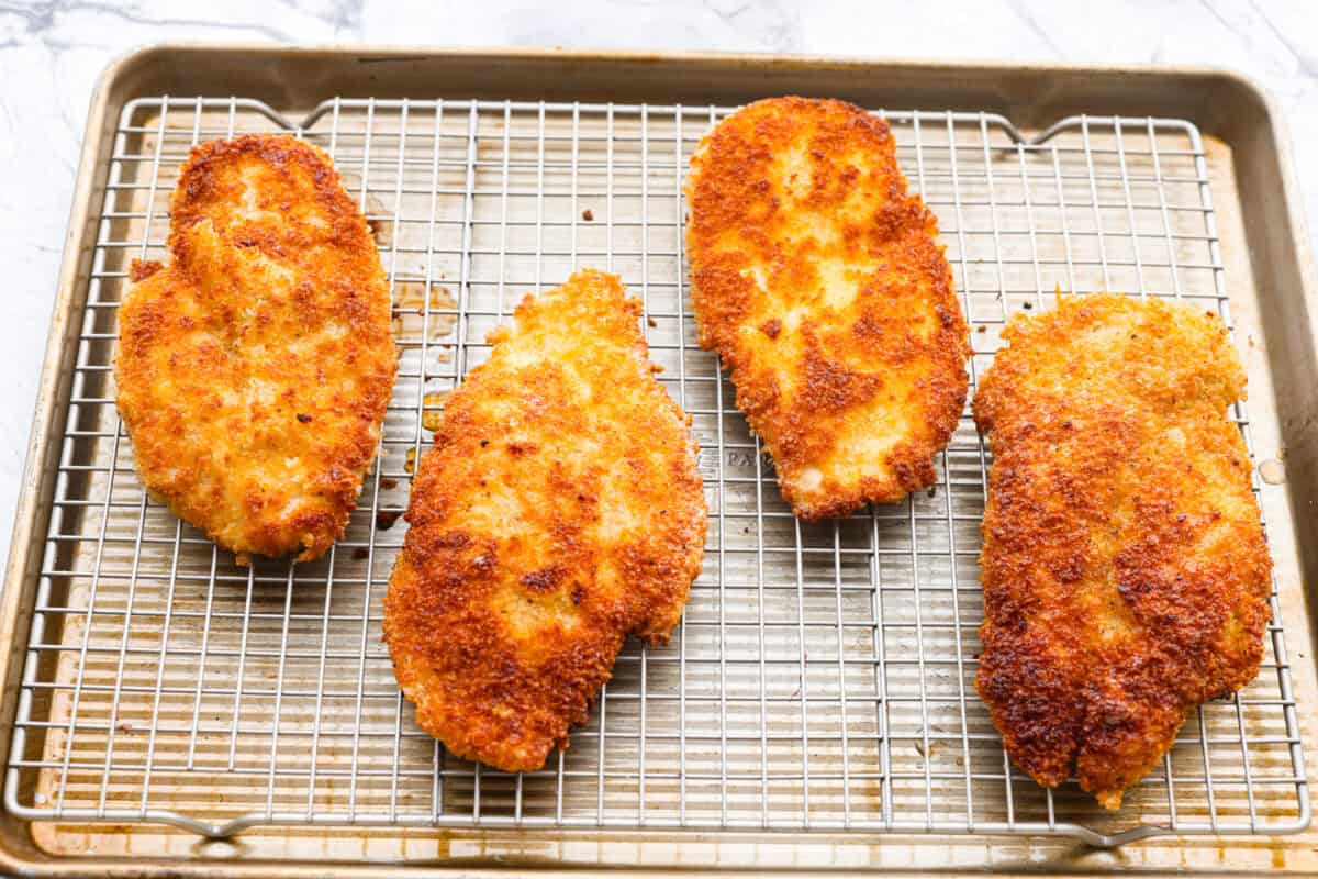 Chicken schnitzel will win you over at first crunch! Thin-pounded, perfectly seasoned chicken is fried to a golden crisp. It’s a timeless, flavor-packed dish that will have your whole family coming back for seconds. Cooked chicken on a wire rack.