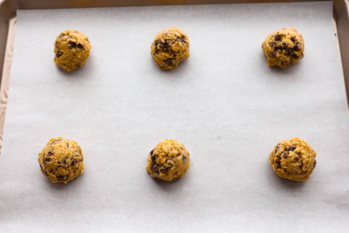 These Neiman Marcus Chocolate Chip Cookies come with a famous backstory, but the real star is the cookie itself. Thick, chewy, and packed with oats, two kinds of chocolate, and crunchy walnuts, theyโre truly worth the hype. cookie dough balls added to a cookie sheet ready to be baked.