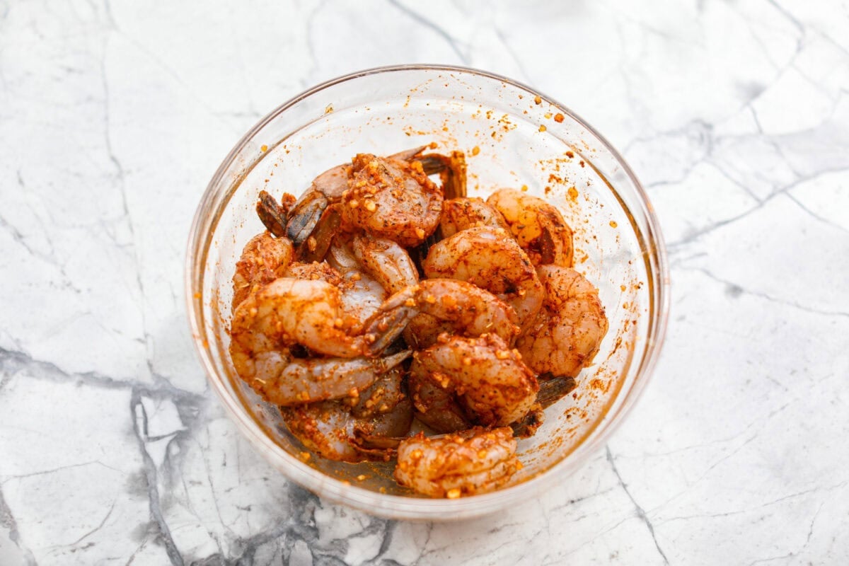 You have to make this New Orleans BBQ shrimp! The shrimp are tender and swimming in a rich, buttery garlic sauce. Grab a bib, lick your fingers, and sop up every last drop with crusty bread. Raw shrimp covered in seasonings in a mixing bowl.