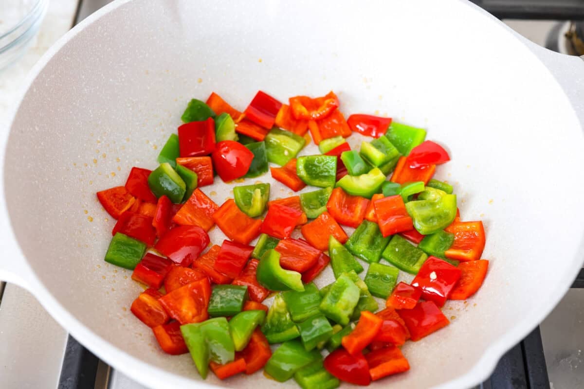 Trust me on this one. If you want the most tender pepper steak you’ve ever made at home, this recipe is it. It’s fast, saucy, and I give you just enough tips to make it work on a busy night! Wok with green and red bell peppers cooking.